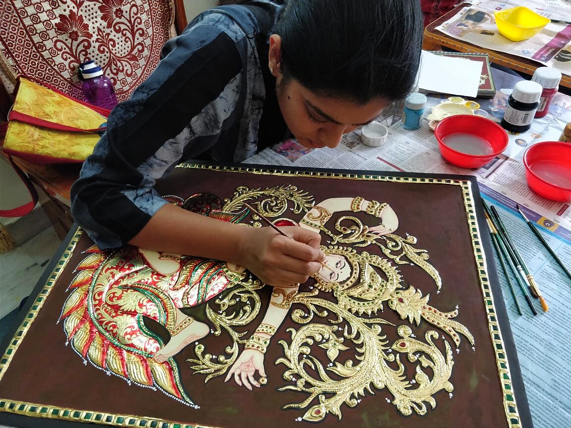 Close-up of a student's hands working gold foil onto a Tanjore painting